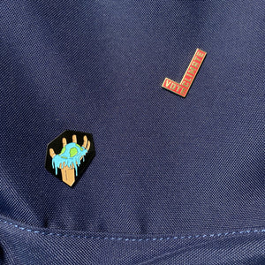 two pin badges on a blue backpack. one pin reads "vote climate" and the other features a hand holding a melting earth.
