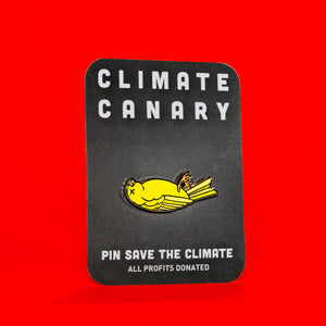picture of an enamel pin on a card. the enamel pin features an illustration of a dead yellow canary laying on it's back with an "x" where the eye would be. the card text reads "climate canary" and "pin say the climate" "all profits donated"