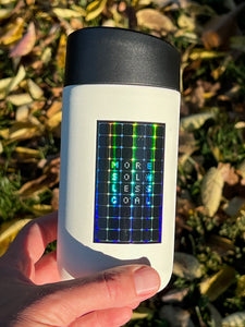 a hand holding a travel coffee mug with a sticker on it. The sticker features a holographic solar panel with text that reads "more sol, less coal"