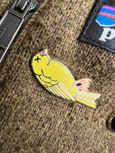 Load image into Gallery viewer, a picture of an enamel pin on a Patagonia sweater. the enamel pin features an illustration of a dead canary lying on its back with an &quot;x&quot; through the eye. 